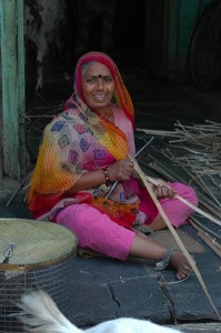 A brightly-dressed woman weaving a basket.