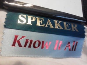 Ribbons on a name tag read, "Speaker. Know-it-all."