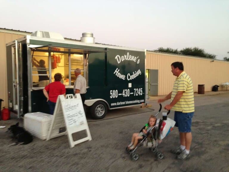 A food trailer is being visited by customers in a parking lot