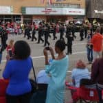 A diverse crowd watches a marching band in a small town parade
