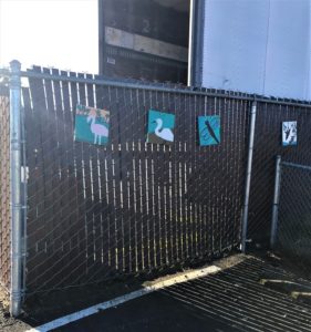 A few art squares hang from a chain link fence