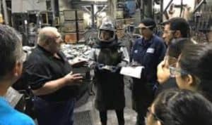 A diverse group dressed in protective equipment tours a foundry