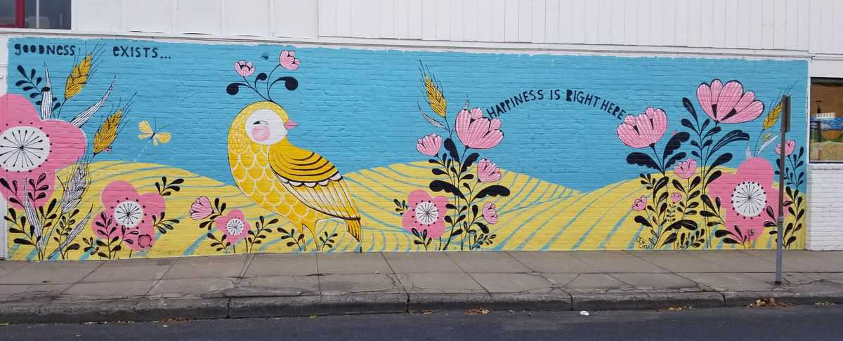 "Goodness exists" and "Happiness is right here" are written on a modern, bright-colored mural with native wildlife and flowers over a landscape of the Palouse area of Washington State.