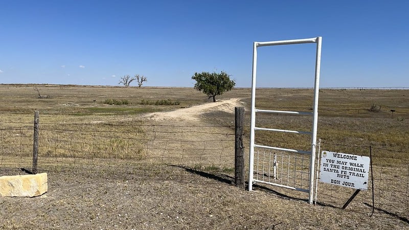 Wide view of a prairie landscape with a walk-through gate in a fence