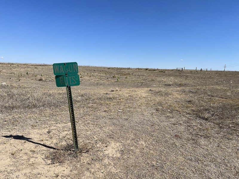 Flat prairie landscape with barely discernable ruts and a sign that says "Wagon ruts"