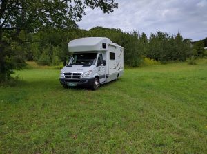 A van-sized RV parked in a green field under trees at a winery