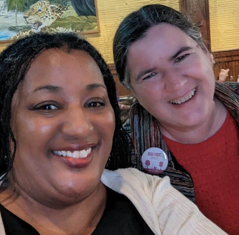 Two women smiling in a selfie. One is wearing a pinback button that says, "OU IQC 2023"