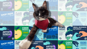A cat wearing a plaid bandana shown over a background of Shop Indie Local graphics