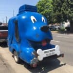 A trailer made in the shape of a big blue dog has a sign that says "mobile grooming"