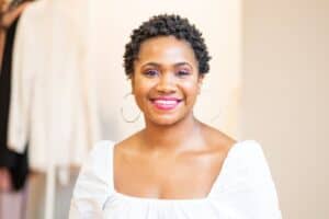 A woman smiling at the camera while standing in front of a clothing rack