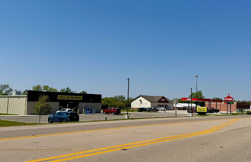 Dollar General on the left and Casey's on the right - directly across from each other, on the main highway in front of them that goes through town. Empty parking lot in front of Dollar General under a blue sky.